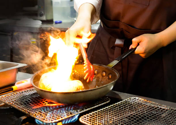 istock Chef cooking with flame in a frying pan on a kitchen stove, Chef in restaurant kitchen at stove with pan, doing flambe on food 1129288734