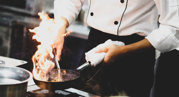 istock Chef cooking with flame in a frying pan on a kitchen stove, Chef in restaurant kitchen at stove with pan, doing flambe on food 1129288769
