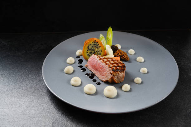 istock menu main course with roasted veal, morels and vegetables on a blue gray plate on a dark table, copy space 1129294908