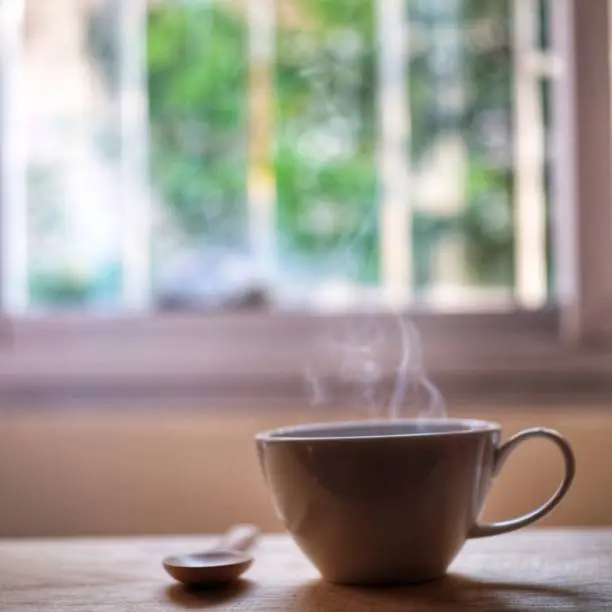 a cup of hot coffee steam smoke on wood table with window background.