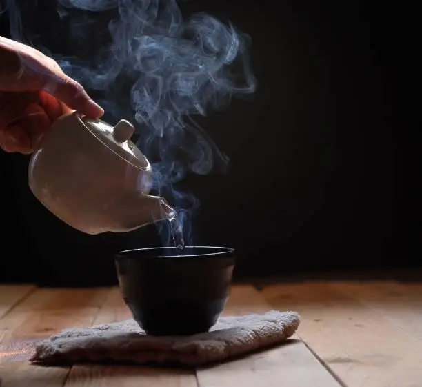 Pouring tea in teapot and cup with steam on wood background. Winter tea time.