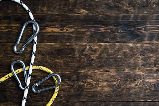 Carabiners and safety rope on a brown wooden board background with copy space.