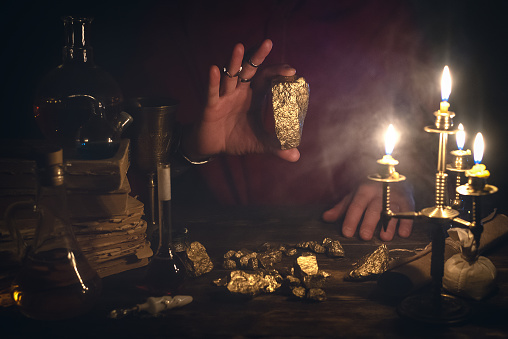 Alchemist is working at his magic table and producing a gold from a stones.