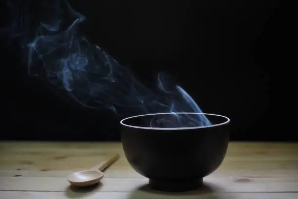 Hot soup in bowl with smoke on wood table and black background.selective focus.