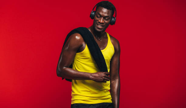 Fitness man relaxing after workout Fitness man with towel on shoulder listening to music on headphones. Fit young man resting after from workout on red background. gym men africa muscular build stock pictures, royalty-free photos & images