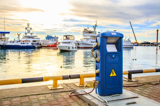 Electric outlets to charge ships and boats at dock. Charging station for boats, electrical outlets to charge ships in harbor - supply electricity for recharging of battery on shore in marina jetty. Electrical power sockets bollard point on pier near sea coast. Luxury yachts docked in port at sunset. sochi photos stock pictures, royalty-free photos & images