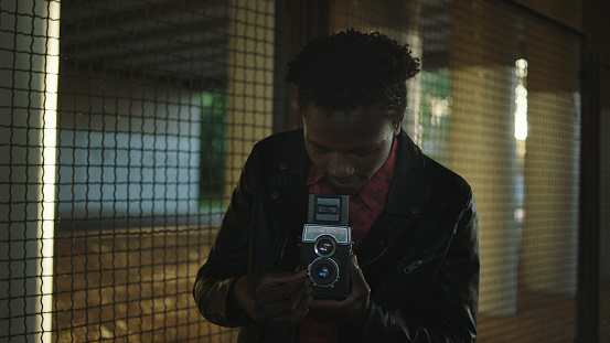 African ethnicity man making photo with old school camera. Under bridge