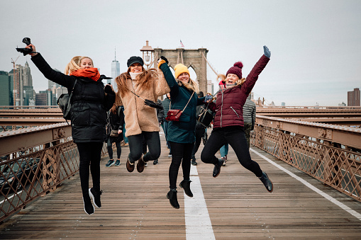 Four women jumping together for a photo on Brooklyn Bridge.