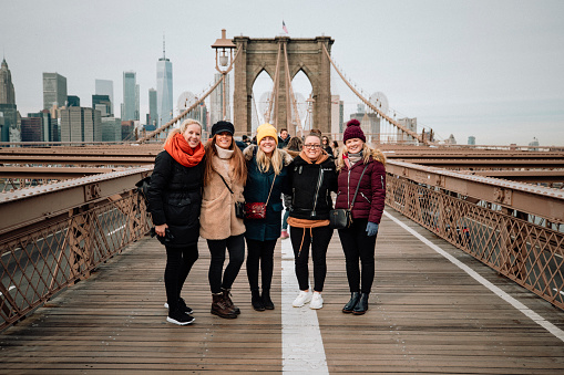 Five women standing side-by-side for a photo on Brooklyn Bridge, New York City.