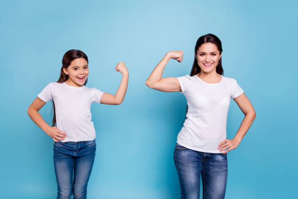 cerrar foto marrón dos personas mamá mamá pelo pequeña hijita una mano en el bíceps que corren a las niñas del mundo fondo azul brillante aislada de la camisetas de ropa blanca - super powers fotografías e imágenes de stock