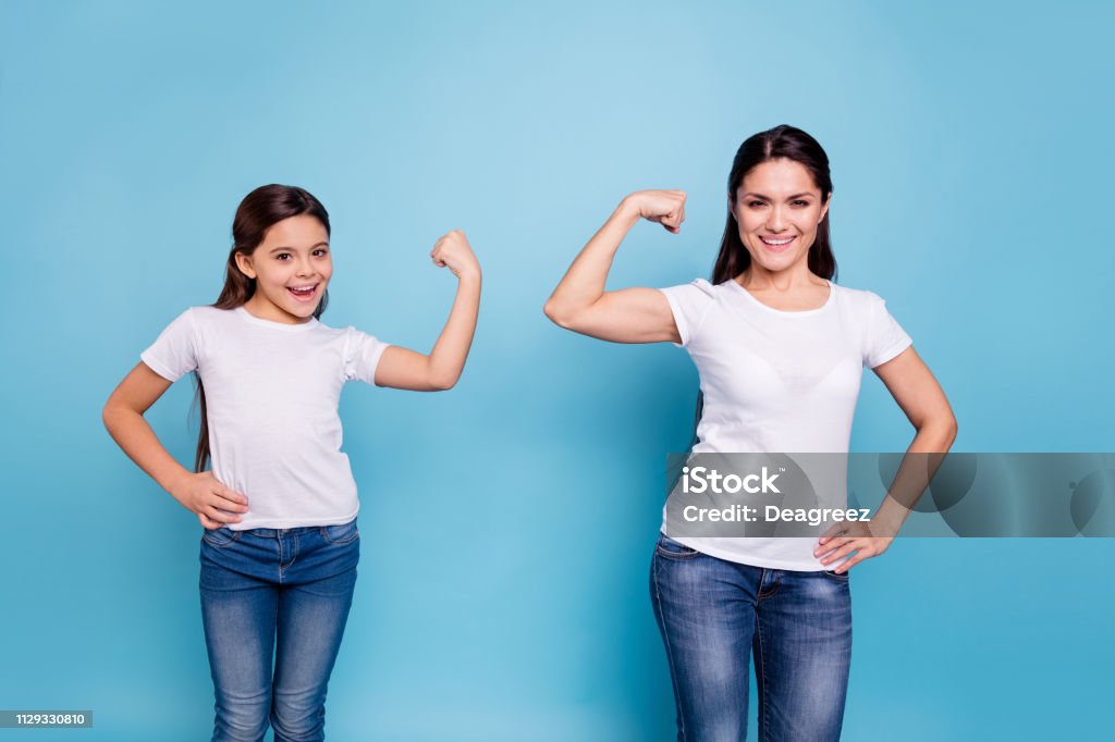 Close up photo two people brown haired mum mom small little daughter hand on biceps who run world girls wear white t-shirts isolated bright blue background Mother Stock Photo
