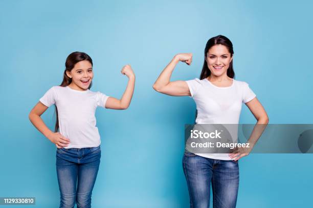 Close Up Photo Two People Brown Haired Mum Mom Small Little Daughter Hand On Biceps Who Run World Girls Wear White Tshirts Isolated Bright Blue Background Stock Photo - Download Image Now