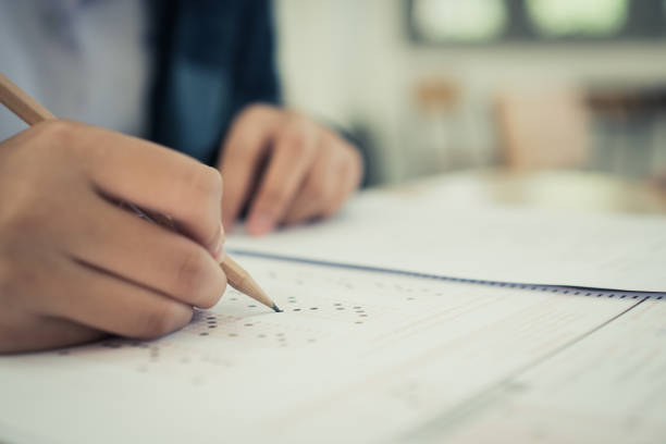 istock Education test concept : Hands with blue pen over application form, Students taking exams, writing examination room with undergraduate inside. Student sitting learning lessons doing final in classroom 1129331316
