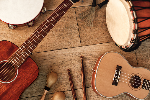 Ethnic musical instruments set: tambourine, wooden drum, brushes, wooden sticks, maracas and guitars laying on wooden floor. Music concept. Musical instruments.