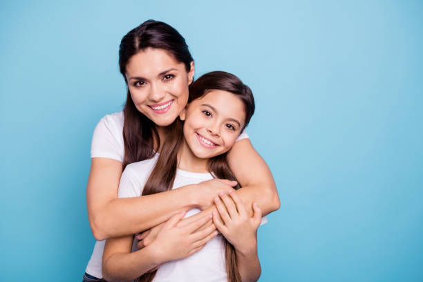 cerrar foto increíble stand de pequeña hijita de mamá mamá pelo marrón bastante dos personas abrazando tiempo libre regreso hermosa alcancía regocijan vistiendo camisetas blancas aislado sobre fondo azul brillante - happy time fotografías e imágenes de stock