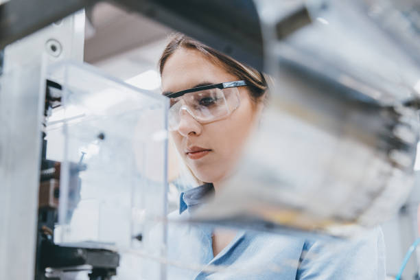 Female industrial worker working with manufacturing equipment in a factory Professional young industrial factory woman employee working with machine parts putting, checking and testing industrial equipments cables in large Electric electronics wire and cable manufacturing plant factory warehouse protective eyewear stock pictures, royalty-free photos & images