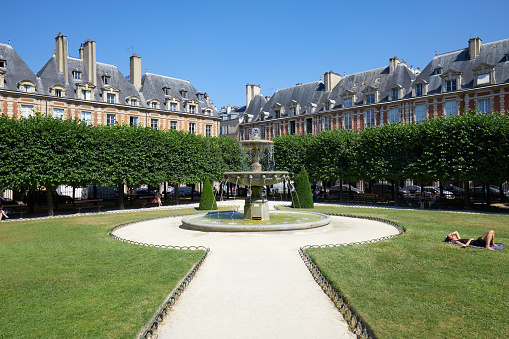 Paris, France - July 6, 2018: Place des Vosges with people on grass and bench in a sunny summer day, clear blue sky in Paris