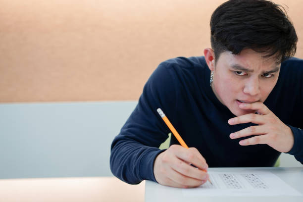 da vicino studente adolescente delle scuole superiori aggrottò la magra e sente stress e pensiero duro dopo aver letto domande sull'esame del test sat in classe, concetto educativo - scholastic aptitude test foto e immagini stock