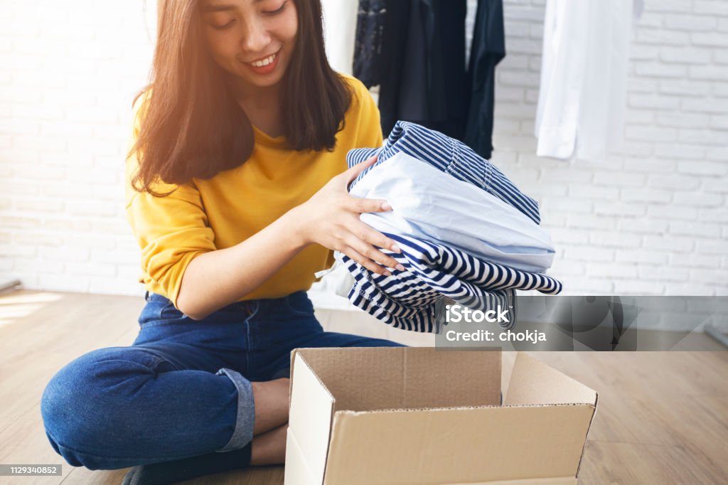 Woman holding Clothes with Donate Box In her room, Donation Concept. Clothing Stock Photo