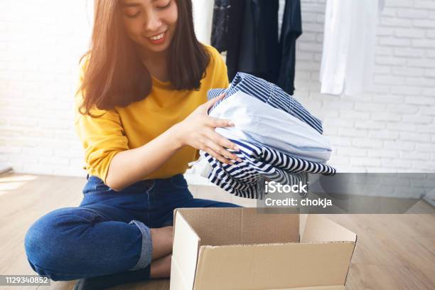 Woman Holding Clothes With Donate Box In Her Room Donation Concept Stock Photo - Download Image Now