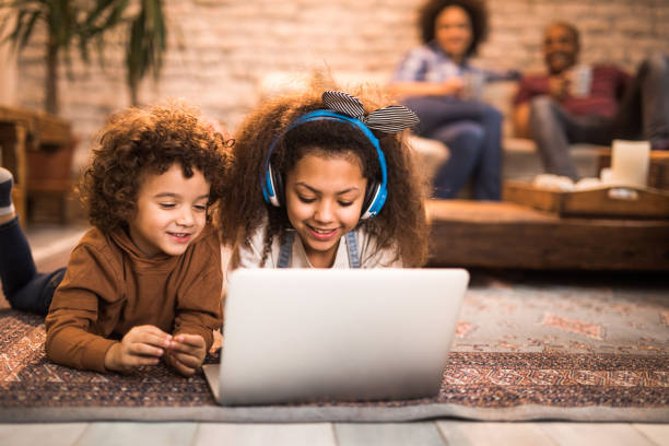istock Happy African American siblings using laptop on carpet at home. 1129341874