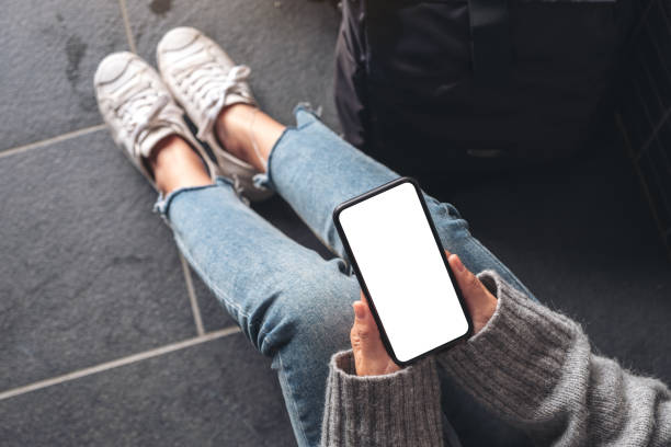 istock Top view mockup image of a woman holding black mobile phone with blank desktop screen while sitting on the floor with baggage 1129341937