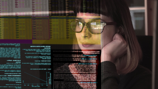 Stock photograph of a pretty young woman concentrating on a see through screen carrying a variety of data.