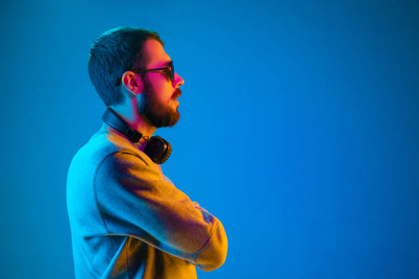 Enjoying his favorite music. Enjoying his favorite music. Serious young stylish man in sunglasses with headphones listening sound while standing against blue neon background dance  electronic music photos stock pictures, royalty-free photos & images