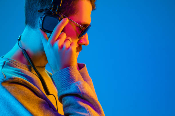 Enjoying his favorite music. Enjoying his favorite music. Serious young stylish man in sunglasses with headphones listening sound while standing against blue neon background dance  electronic music photos stock pictures, royalty-free photos & images