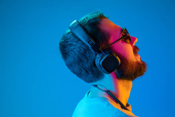 Enjoying his favorite music. Enjoying his favorite music. Happy young stylish man in sunglasses with headphones listening and smiling while standing against blue neon background dance  electronic music photos stock pictures, royalty-free photos & images