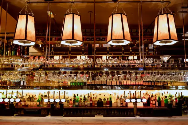 Wide angle shot of a restaurant interior of the bar counter and shelves of alcohol behind the bar.