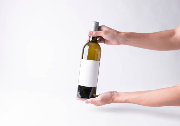 istock Hand holding a wine bottle for mock-up. Blank Label on a gray background. 1129343939
