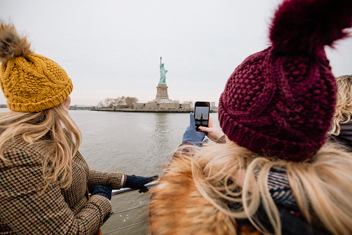 Two women photographing the Statue of Liberty from a tour boat in New York City.