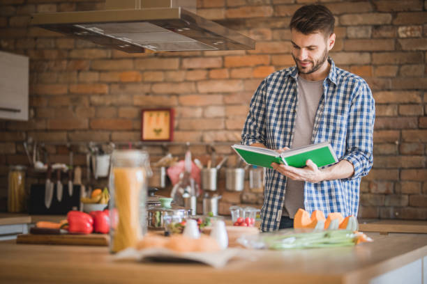 Smiling man using cookbook for preparing food in the kitchen.