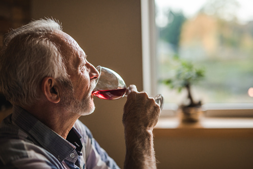 Pensive mature man drinking red wine at home and looking away.