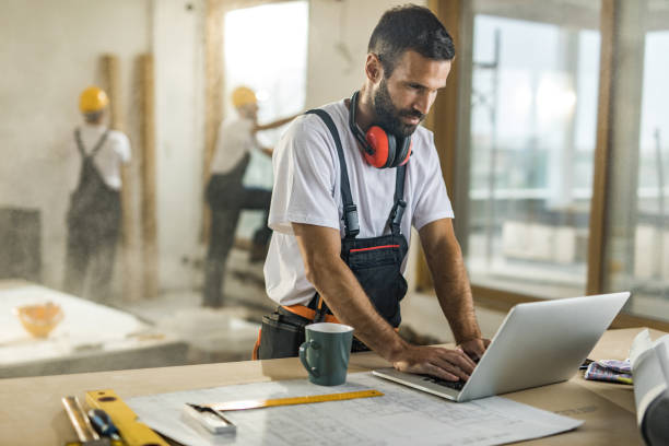 arbeiter, die mit hilfe eines computers auf baustelle lächelnd. - building contractor computer internet construction worker stock-fotos und bilder