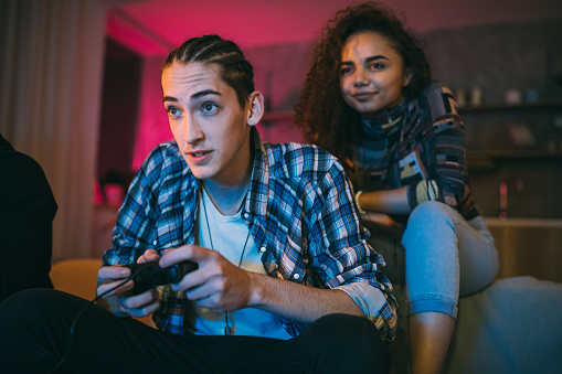 Young man playing video games, Young beautiful woman sitting behind him and cheering his boyfriend