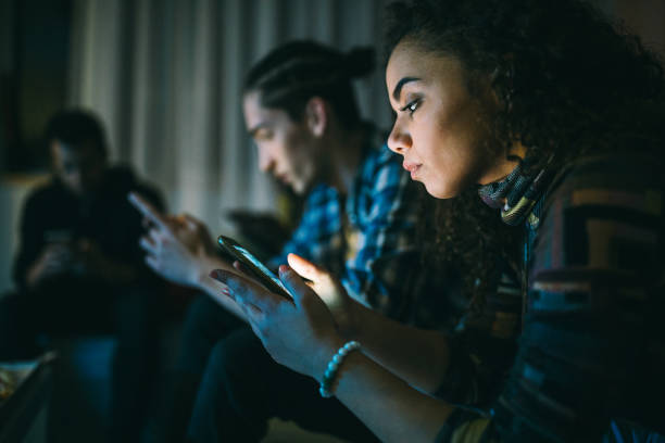 amigos que usan teléfonos inteligentes mientras están sentados juntos - african descent addiction african ethnicity rudeness fotografías e imágenes de stock