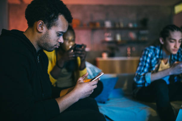 amigos que usan teléfonos inteligentes mientras están sentados juntos - african descent addiction african ethnicity rudeness fotografías e imágenes de stock