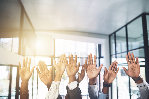 Closeup shot of a group of businesspeople raising their hands in an office