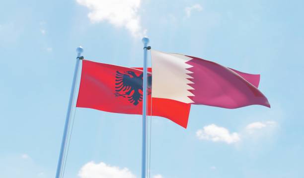 istock Qatar and Albania, two flags waving against blue sky 1129350124