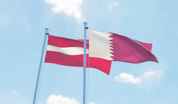 istock Qatar and Latvia, two flags waving against blue sky 1129350689