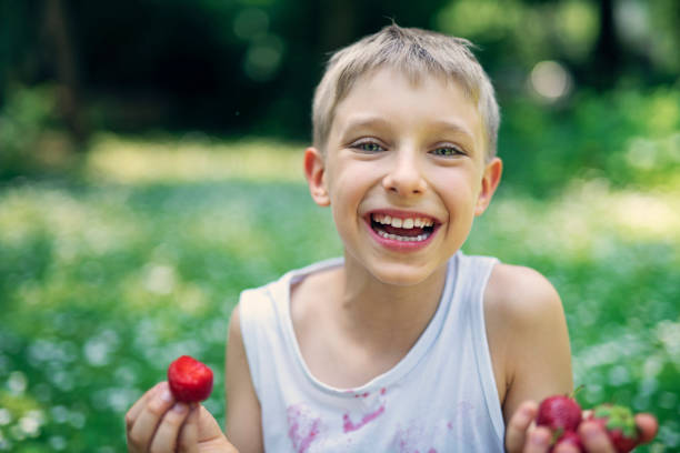 Happy little boy sitting on grass and eating strawberries. \nNikon D850