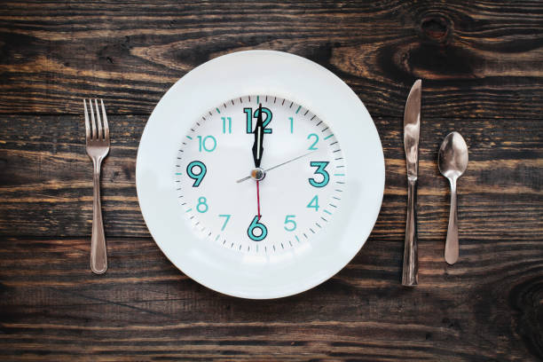 concepto tiempo ayuno intermitente del doce horas con el reloj en la placa - ayuno intermitente fotografías e imágenes de stock