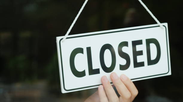 The hand turns the sign with the inscription open to the Closed position. The end of the working day The hand turns the sign with the inscription open to the Closed position. The end of the working day. close stock pictures, royalty-free photos & images