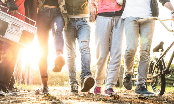 amigos caminando en el parque de la ciudad con luz de fondo y sunflare halo - concepto de amistad milenaria y multirracial gente joven de moda alternativo que se divierten juntos - vista de pierna con suave movimiento borrosa - city street audio fotografías e imágenes de stock