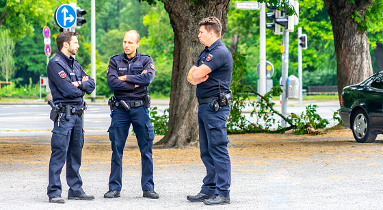 Hannover, Germany, May 19., 2018: Three German policemen in dark blue uniforms are standing with crossed arms on the sidewalk next to a street.