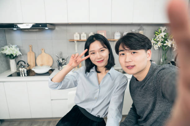 istock Smiling young chinese couple in kitchen taking selfie 1129358815