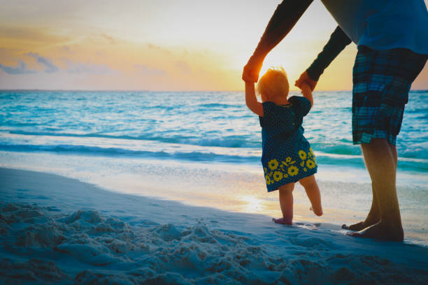 istock father help little daughter to make first steps on sunset beach 1129359390