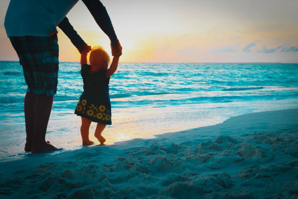 istock father help little daughter to make first steps on sunset beach 1129361134